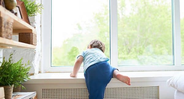 Rear View Of Boy Climbing Up Onto Window Sill